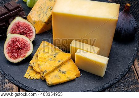 British Matured Yellow Cheese Blue Shropshire, Smoked Cheddar And Fresh Figs Close Up On Black Stone