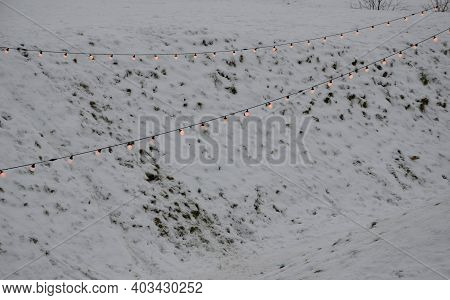 View Of Winter Snowy Slopes Of A Ski Resort With Lit Chains Of Light Bulbs. These Lights Are Used At
