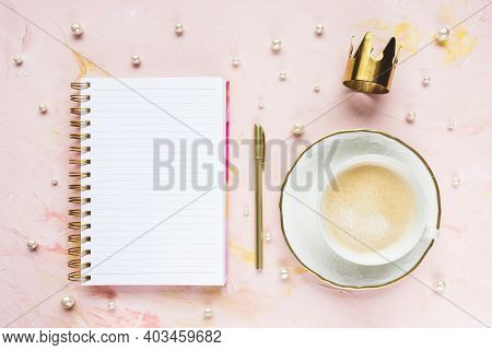 Open Notepad, Pen, Gold Crown And White Pearls Decoration On Woman Desk Workspace, Pink Background. 