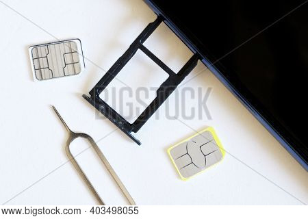 Two Miniature Nano Sim Cards, And A Smartphone With An Removed Tray For Two Empty Slots Lie Next To 