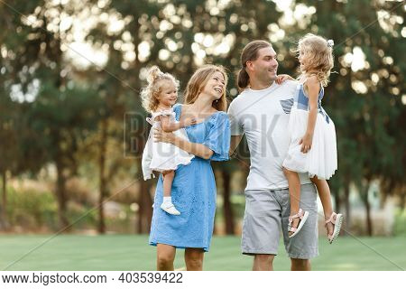 Parents Hold Daughters In Their Arms In Countryside, Enjoing Time Together. Happy Family Concept. Bl