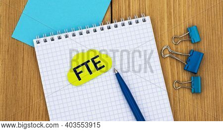 Fte (full Time Equivalent) - Word Written In A Notebook On A Wooden Background With A Pen And Clamps