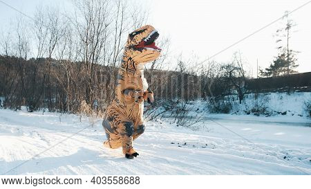 A Man In A Tirex Dinosaur Costume Walks Through The Forest In Winter
