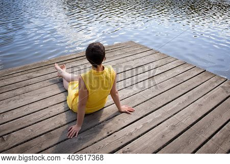 Young Woman With Yellow Dress Relaxing, Sitting By A Lake.