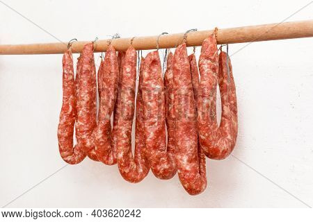 Drying Sausages From Raw Minced Meat In Limbo On A Wooden Stick On A White Wall Background At Home.
