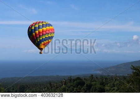 Colorful Hot Air Balloon Fly Over The Blue Sea. Big Blue Hot Air Balloon Flying In Light Blue Sky Wi