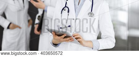 Unknown Woman Doctor Iusing Tablet Computer In Her Hands, While Standing In Clinic. Medicine Concept