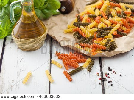Raw Homemade Tricolore Fusilli Pasta In Brown Paper On White Wooden Table Background With Basil And 