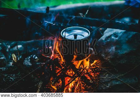 Kettle In Soot Hanging Over Fire. Cooking Food At Fire In Wild. Beautiful Firewoods Burn In Bonfire 