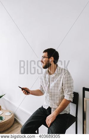 Portrait Of Young Cheerful Caucasian Man In Glasses And Earphones Using Mobile Phone.\n\nman, Busine
