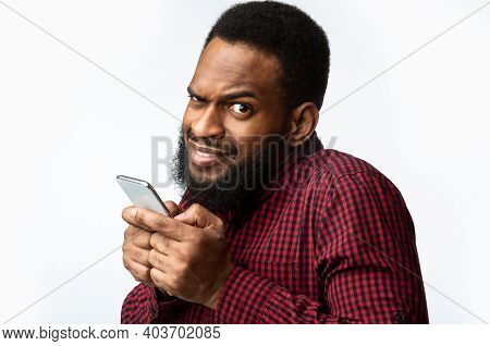 Phone Fraud. Black Man Using Smartphone Looking At Camera Posing Over White Studio Background. Telep