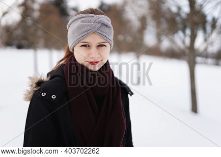 Photo Of Happy Young Girl In Winter Clothes With Snow Looking Right In The Camera.