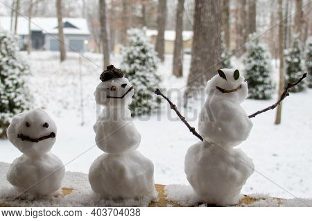 Three  Snow People Sitting On The Deck Railing