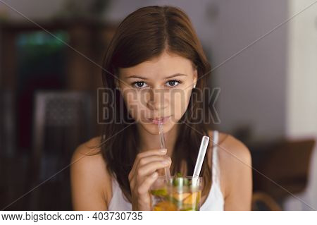Young Girl In Cafe Drinking Cold Lemonade With Fruit