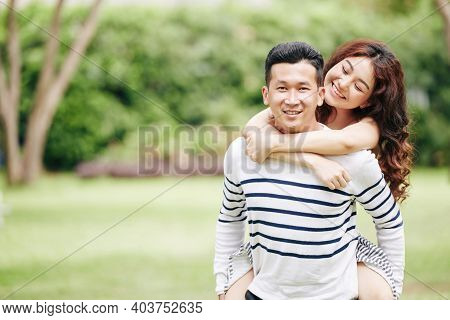 Pretty Happy Young Asian Woman Hugging Her Boyfriend From Behind When Thay Are Standing In Local Par