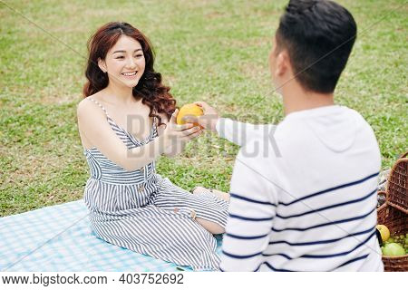 Happy Beautiful Young Woman Taking Orange From Hands Of Her Boyfriend When Thay Are Having Picninc I