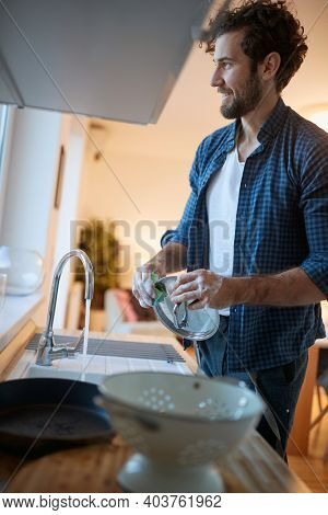 A diligent young man doing housework in a relaxed atmosphere in the kitchen. Kitchen, housework, quarantin, home