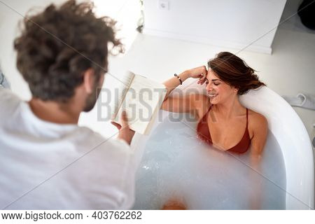 A young sexy girl enjoying a bath while a boyfriend reading a book to her in a relaxed atmosphere of the bathroom. Love, relationship, together