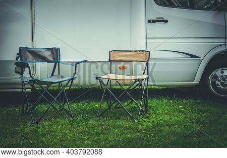 Campsite And Summer Recreation Theme. Two Empty Camping Deckchairs In Front Of Rv Camper Van Recreat