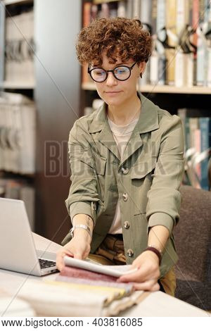 Young female manager of studio of interior design using laptop while looking through new samples of fabris for making furniture