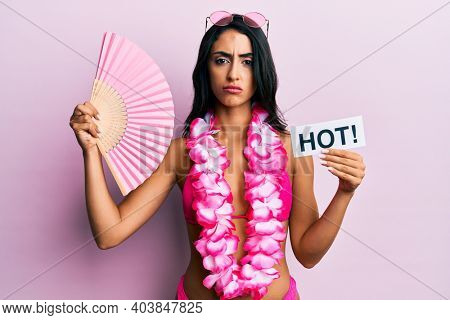 Beautiful hispanic woman wearing bikini and handfan holding hot word skeptic and nervous, frowning upset because of problem. negative person. 