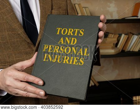 Hands Holding A Book Torts And Personal Injuries Law Book.