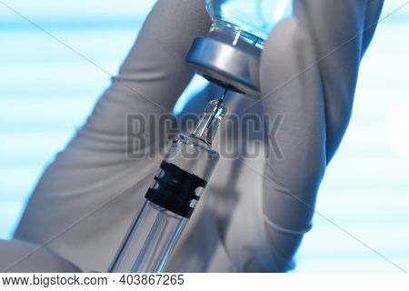 Woman Filling Syringe With Vaccine From Vial On Blurred Background, Closeup