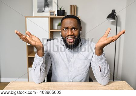A Young And Handsome African-american Employee Is Sitting At The Desk And Raising His Hands Up, Feel