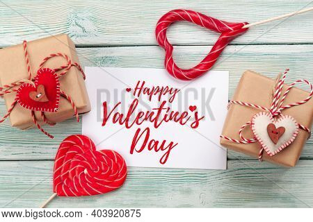 Valentines day greeting card. Gift boxes and heart candy sweets over wooden background. Top view flat lay