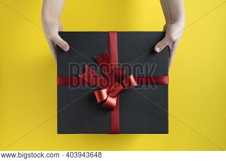 Hands Are Holding Large Black Box With Red Bow. Top View. Gift For Man
