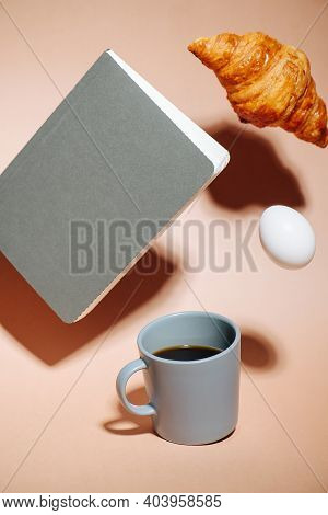 Breakfast Concept. Coffee Mug, Croissant, Egg And Notebook Hovering In Air