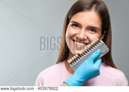 Doctor Checking Young Woman's Teeth Color On Light Grey Background. Cosmetic Dentistry