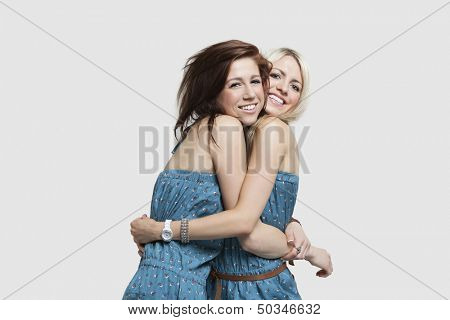Two young women in matching jump suits embracing each other over gray background