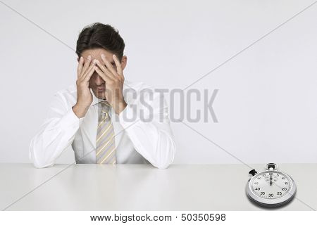 Worried businessman at table with stopwatch representing loss of time