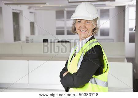 Portrait of smiling senior woman in reflector vest and hard hat at office
