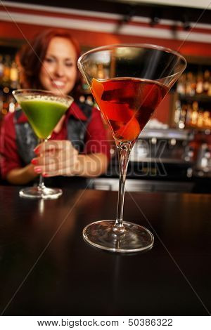 Cheerful barmaid with cocktail behind bar counter 