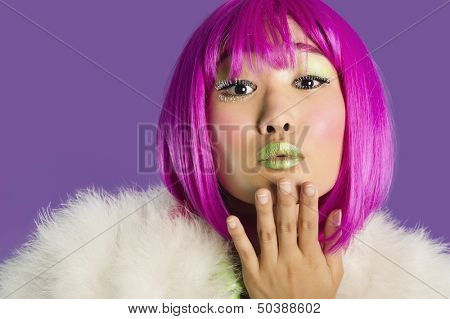 Portrait of young funky woman in pink wig blowing kiss over purple background
