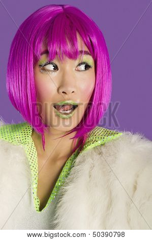 Surprised young funky woman in pink wig looking sideways over purple background