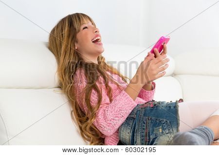 Blond kid girl playing fun with mobile smartphone on white sofa byod