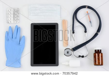 High angle shot of a group of medical / health care related items including: Stethoscope, tongue depressors, latex glove, medicine, pills, mask, syringe and a Tablet Computer, with blank screen.