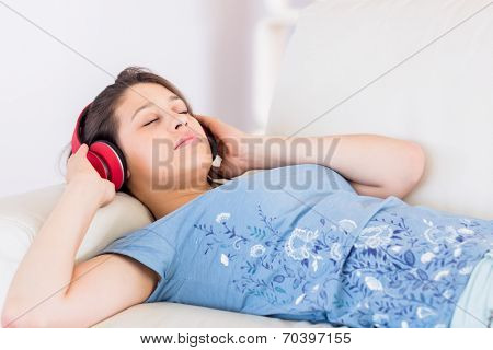 Pretty brunette listening to music on the couch at home in the living room