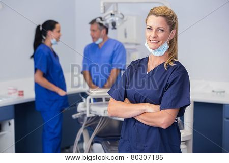 Smiling nurse with arms crossed and co-workers behind her