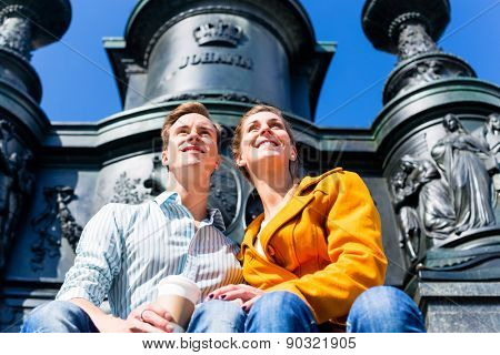 Tourist couple sitting in Dresden Theaterplatz in front of statue