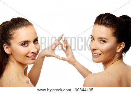 Two beautiful women making heart with fingers.