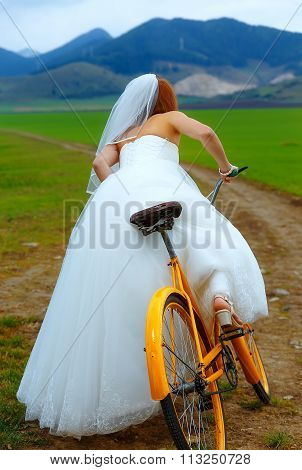 bride on orange bike in beautiful wedding dress with lace in landscape. wedding concept.