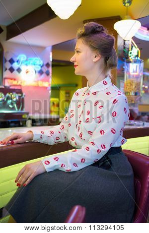 Profile of beautiful girl in blouse with red lips at the bar with yellow lights.