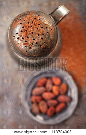 vintage sifter with cocoa beans on old backing metal background
