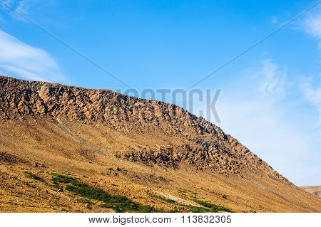 Rocky Dry Yellow Cliff Slope Against Light Blue Sky