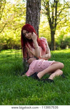 Young and beautiful ukrainian girl  with red hair sits under the tree in the park