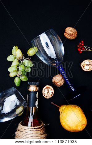 The still life with white wine in glass bottle on black background. Glasses of wine with fresh grape